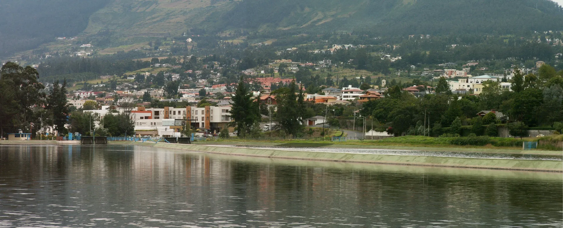 Cumbayá desde el reservorio: casas y conjuntos residenciales entre árboles en la ladera del valle.